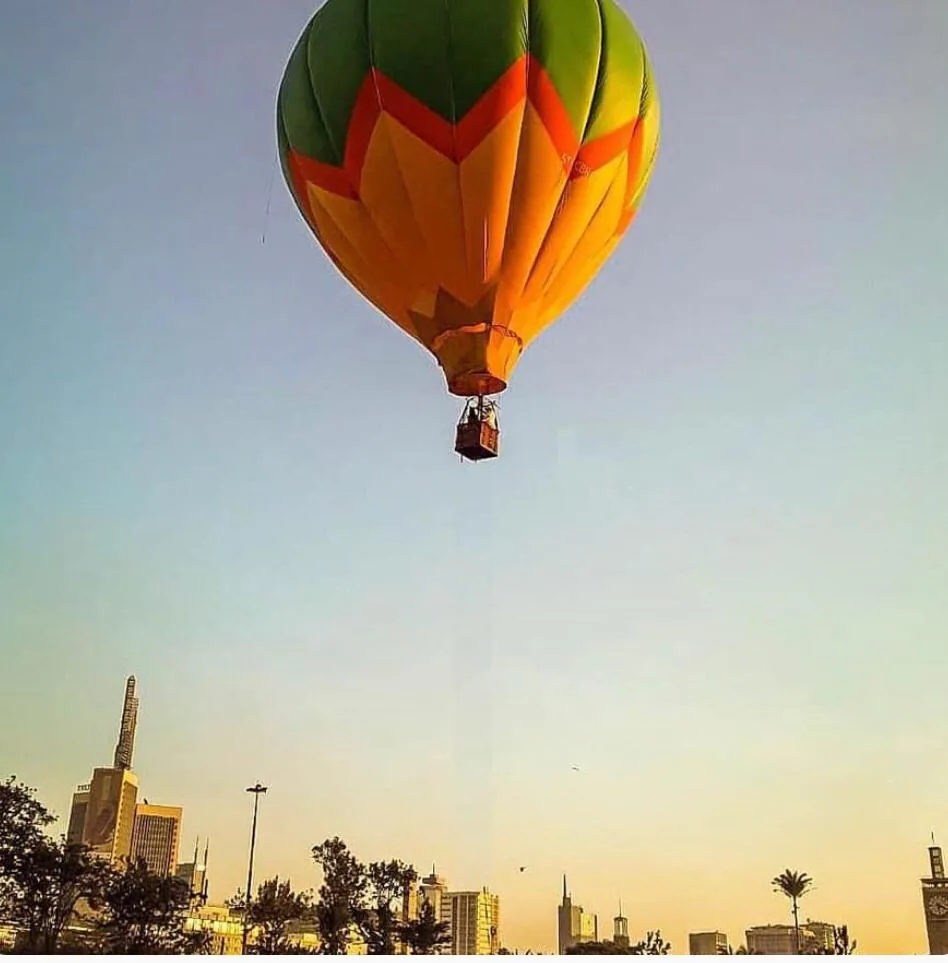 A hot air balloon floats above the Nairobi skyline at dusk, the city's towers and palms silhouetted below