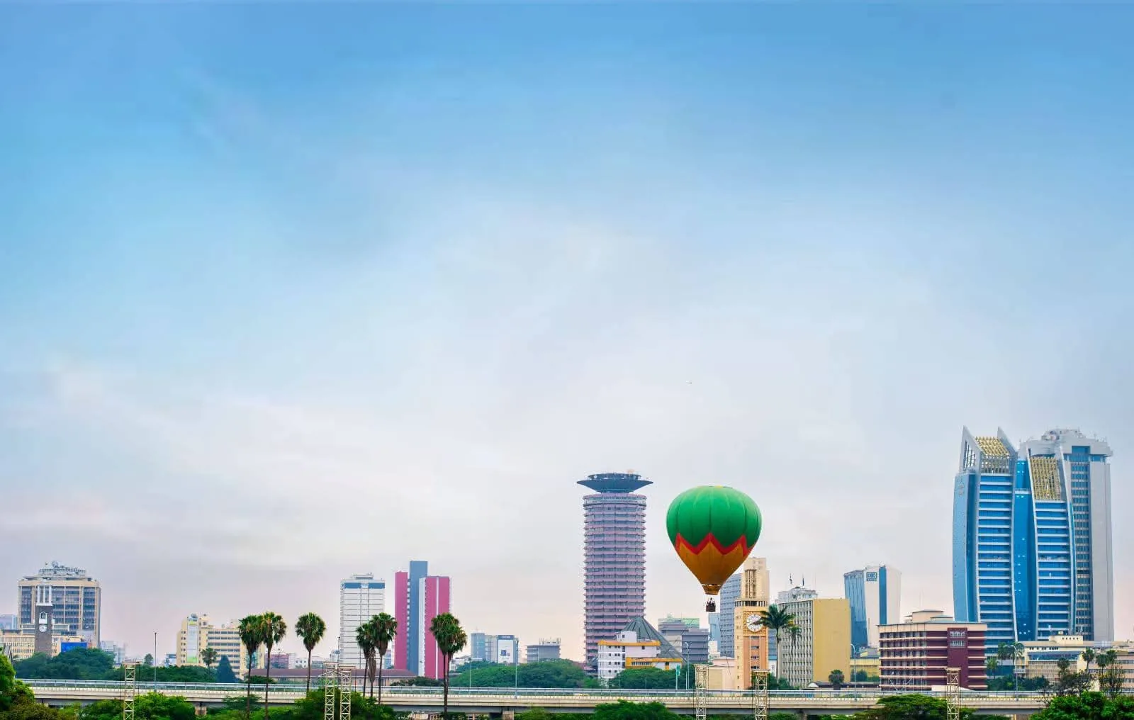A green and orange balloon drifts past the Nairobi skyline in daylight, framed by the KICC tower and glass office blocks