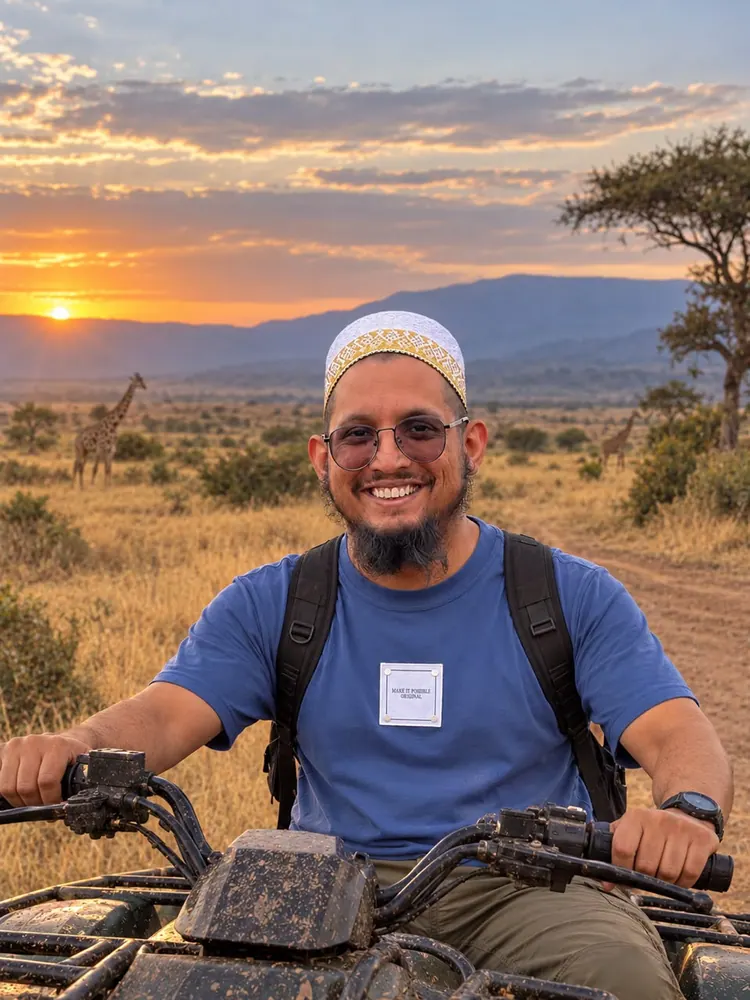 Ruyah Adventures founder Luvai sits at the handlebars of a quad bike at sunset, smiling, with giraffe on the plain behind him