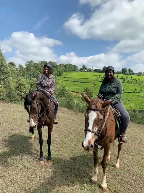 Two smiling riders in helmets on horseback with terraced green tea fields rising on the hillside behind them