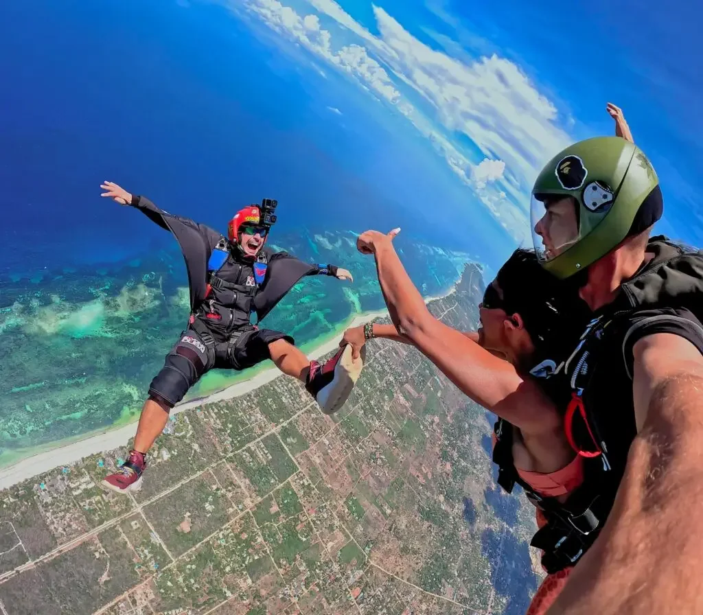 Two skydivers in freefall high above the Kenyan coastline, the reef and ocean far below them